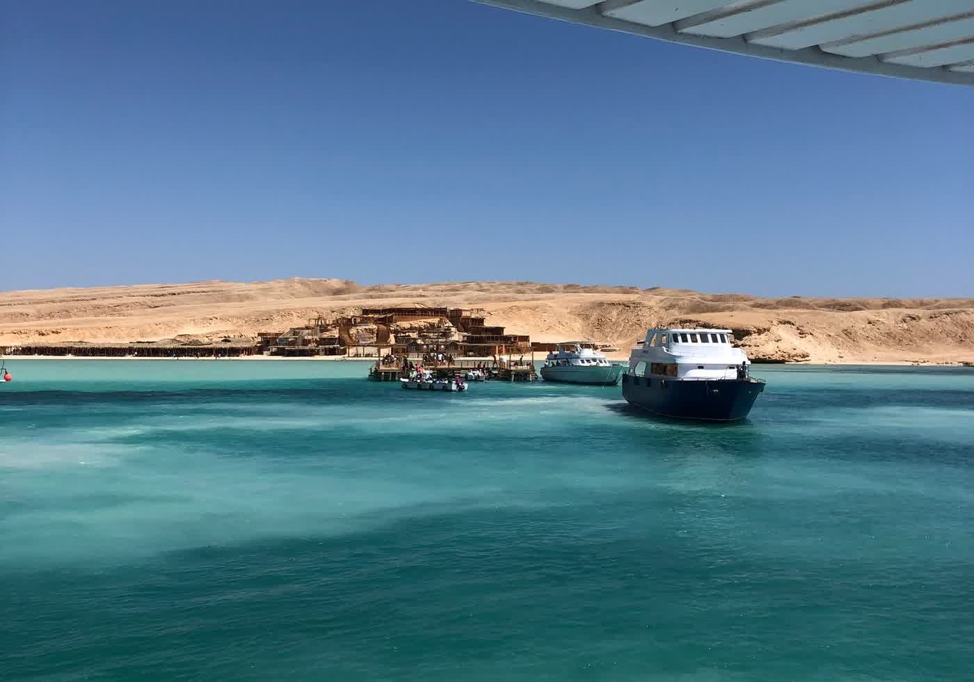 A boat leaving a Red Sea marina, turquoise water and a low desert shore behind it.